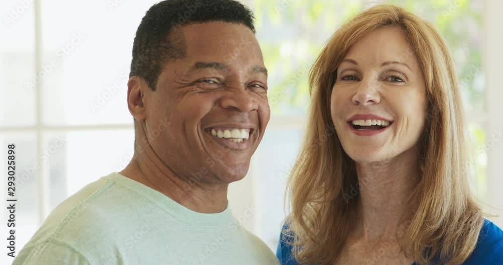 Close up portrait of laughing mixed race senior couple looking at each other then turning to camera. Happy older African American Husband and Caucasian wife at home. Slow Motion 4k Handheld Close up portrait of laughing mixed race senior couple looking at each other then turning to camera. Happy older African American Husband and Caucasian wife at home. Slow Motion 4k Handheld