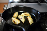 Pan fried dumplings in a cast iron skillet on the stove in a home kitchen.