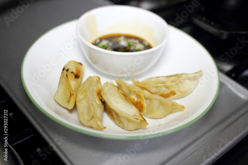 Pan fried dumplings with soy dipping sauce on a plate, resting on the stove top in a home kitchen.