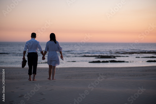 Couple holding hands and walking on beach during sunset