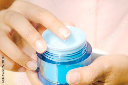 Hand of woman holding moisturizer cream and serum. She applying a facial cream , essential , oil , lotion and body cream for skin care, close up view and blur background. Beauty and Healthy Concept.
