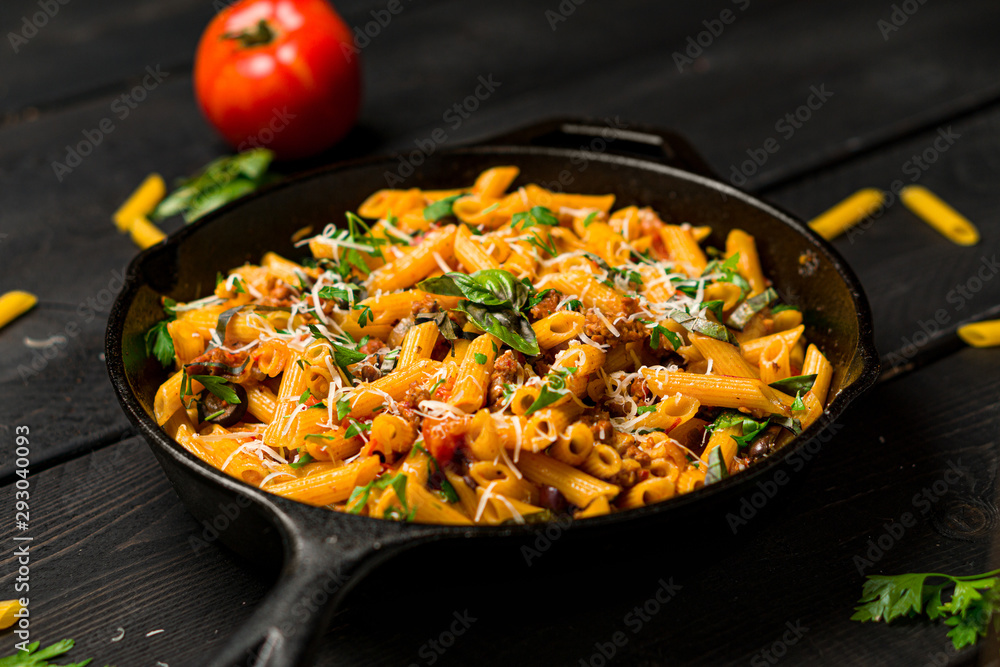 Pasta on dark background. This quick & delicious pasta meal is made with penne pasta, fresh tomato sauce and sausage. This italian inspired comfort food is cooked and served in a cast iron skillet.
