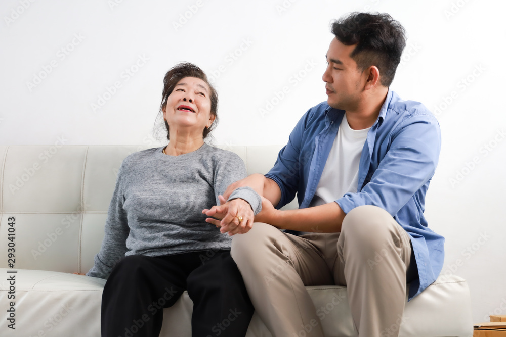 Asian senior woman mother and young man son in blue shirt massage his mother in living room Asian senior woman mother and young man son in blue shirt massage his mother in living room
