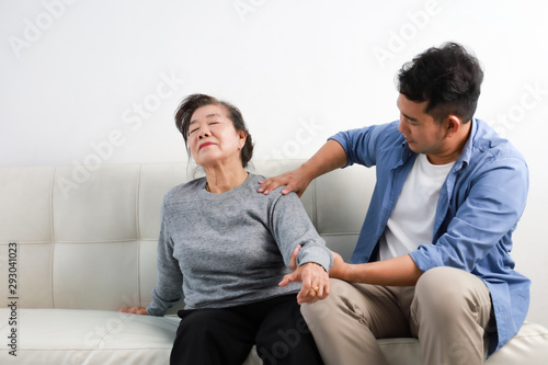 Asian senior woman mother and young man son in blue shirt massage his mother in living room