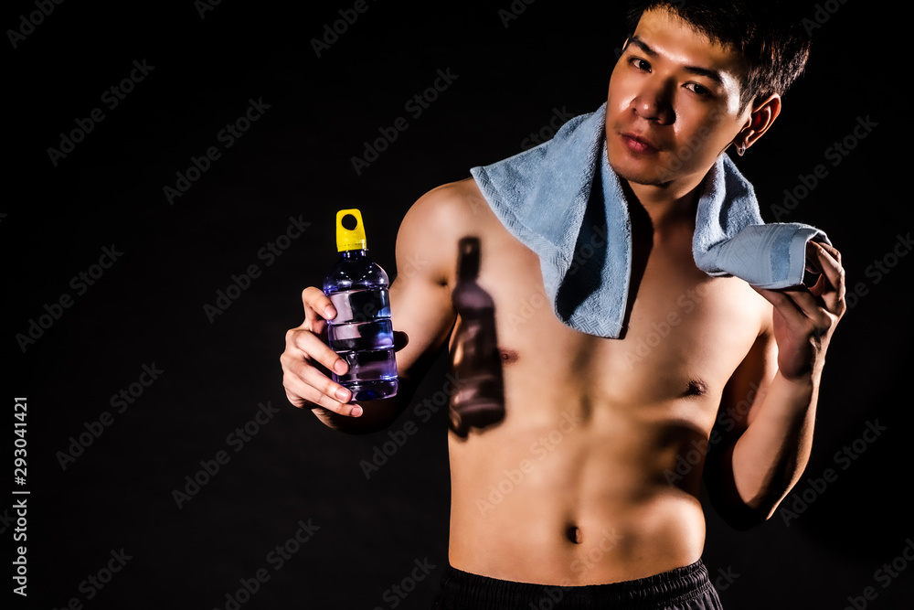 Fototapeta premium sport man standing holding a towel and bottled water on black backgrounds, fitness concept, sport concept