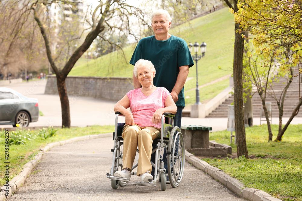 Senior woman in wheelchair and mature man on sunny day outdoors Senior woman in wheelchair and mature man on sunny day outdoors