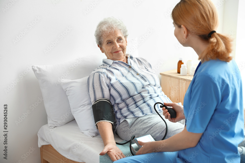 Nurse measuring blood pressure of elderly woman indoors. Medical assistance Nurse measuring blood pressure of elderly woman indoors. Medical assistance