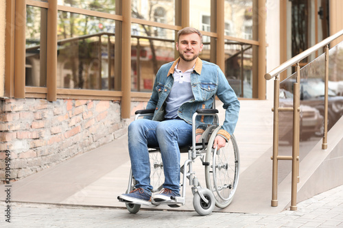 Young man in wheelchair using ramp at building outdoors