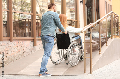 Woman in wheelchair and man using ramp outdoors
