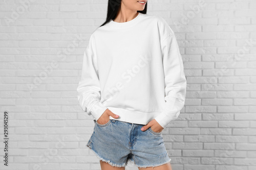 Young woman in sweater at brick wall, closeup. Mock up for design photo