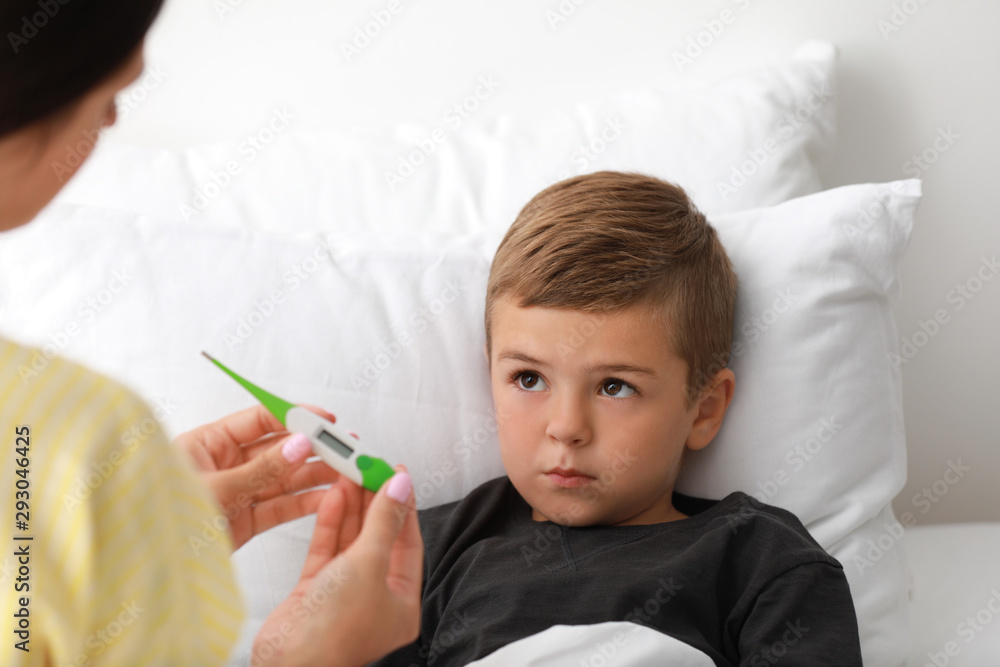 Mother measuring temperature of her sick son in bed Mother measuring temperature of her sick son in bed