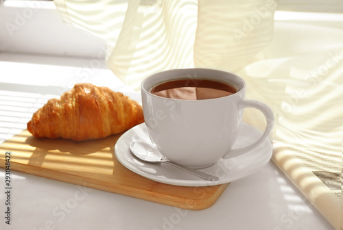 Delicious breakfast with croissant and cup of coffee on window sill