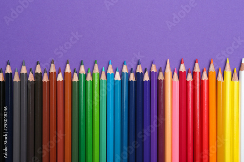 Colorful pencils on purple background, flat lay