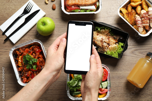 Top view of woman holding smartphone over wooden table with lunchboxes,  mockup for design. Healthy food delivery