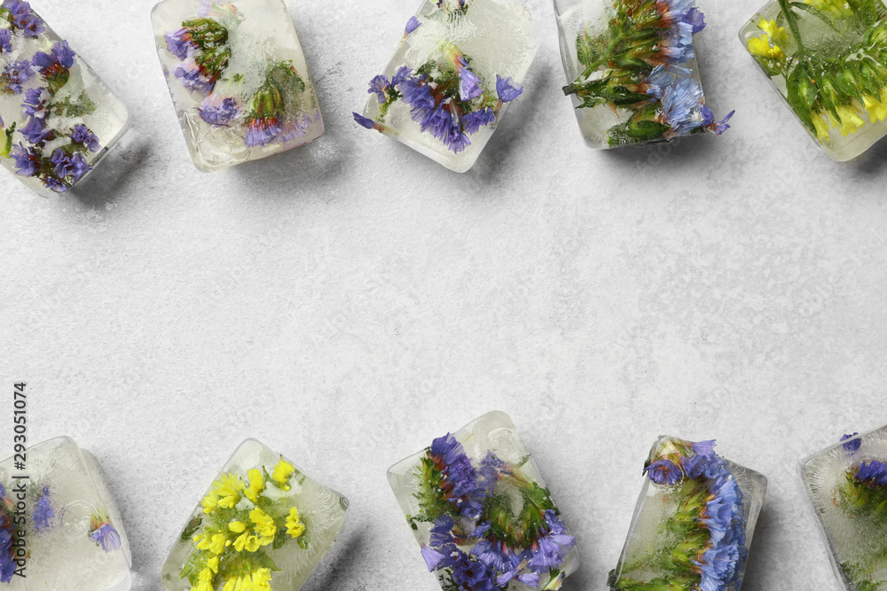 Ice cubes with flowers on light stone background, flat lay. Space for text Ice cubes with flowers on light stone background, flat lay. Space for text
