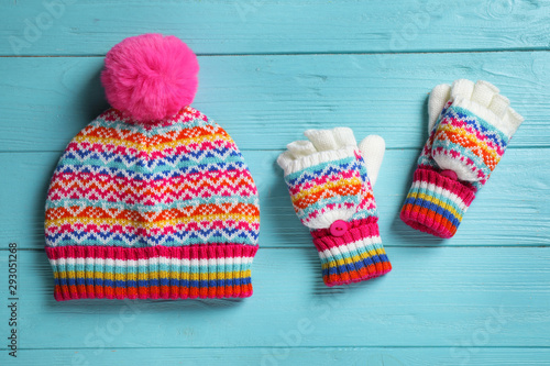 Warm knitted hat and mittens on blue wooden background, flat lay