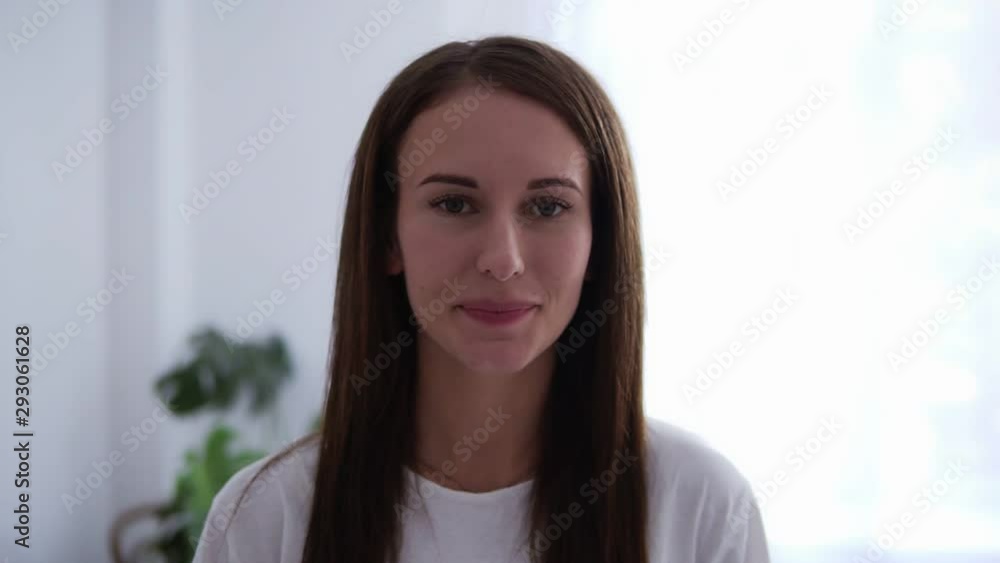 Portrait of beautiful brunette young woman looking at camera and bright light on background inside smiling face casual hairstyle stylish girl beauty charming look. White coloured living room Portrait of beautiful brunette young woman looking at camera and bright light on background inside smiling face casual hairstyle stylish girl beauty charming look. White coloured living room
