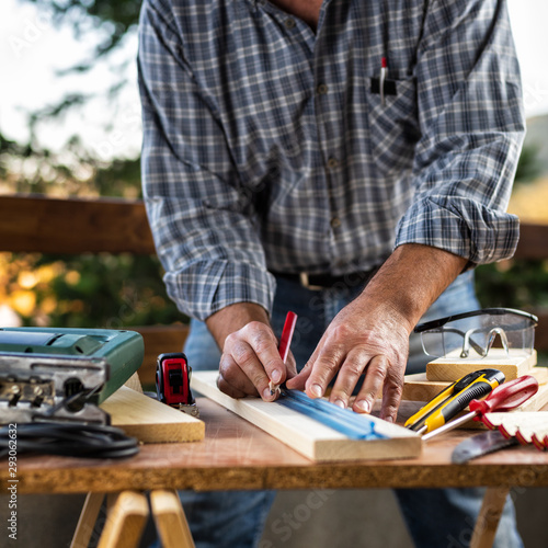 Adult craftsman carpenter with pencil and ruler tracing the cutting line on a wooden table. Housework do it yourself. Stock photography.