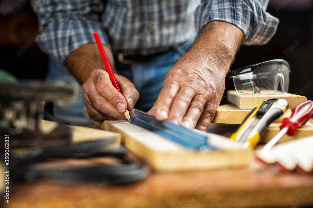 Adult craftsman carpenter with pencil and ruler tracing the cutting line on a wooden table. Housework do it yourself. Stock photography.