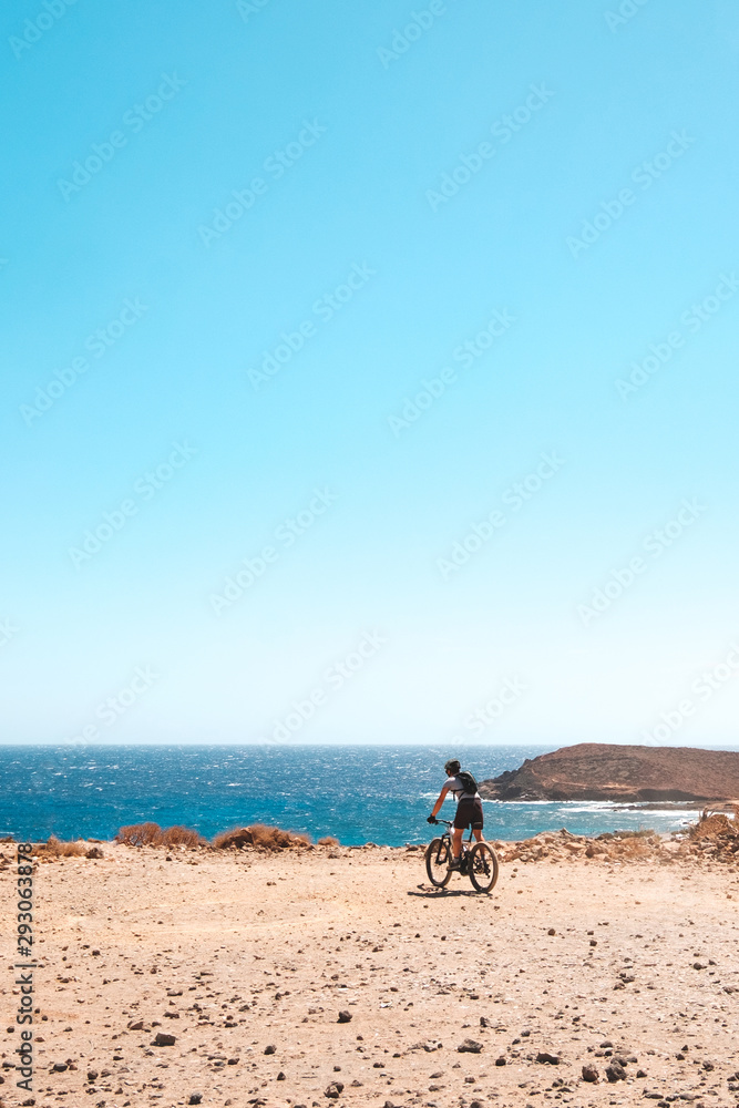 person on mountain bike bicycle in desert landscape near coast with ocean background person on mountain bike bicycle in desert landscape near coast with ocean background