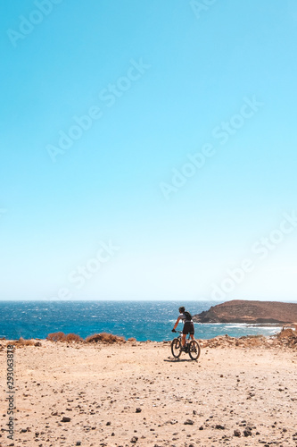 person on mountain bike bicycle in desert landscape near coast with ocean background
