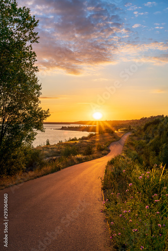 Asphalt road along a lake during a beautiful summer sunset