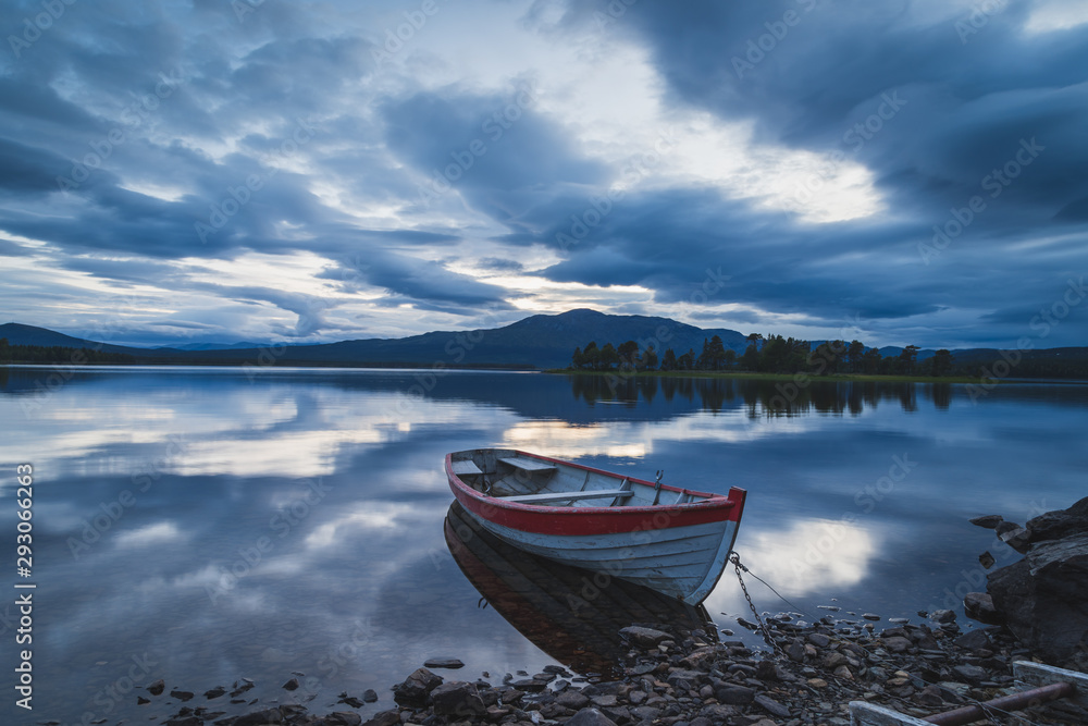 Old rowboat at the rocky shore of a lake on a cloudy evening. Jamtland, Sweden. Old rowboat at the rocky shore of a lake on a cloudy evening. Jamtland, Sweden.
