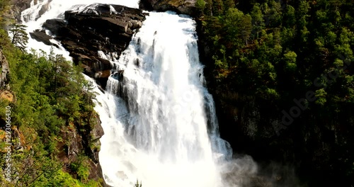 Kinsarvik, Hordaland, Norway. Waterfall Nyastolfossen In Hardangervidda Mountain Plateau. Nyastolsfossen in Spring Sunny Day. Height Of 115 m. Famous Natural Norwegian Landmark And Popular Destination photo