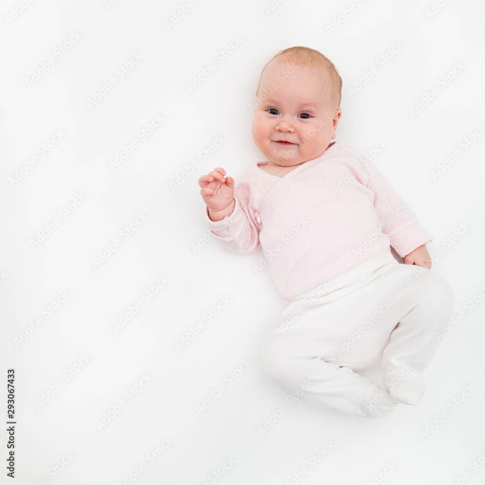 happy baby in white and pink body suit lying on his back on the white. Baby looking straight at the camera. happy baby in white and pink body suit lying on his back on the white. Baby looking straight at the camera.