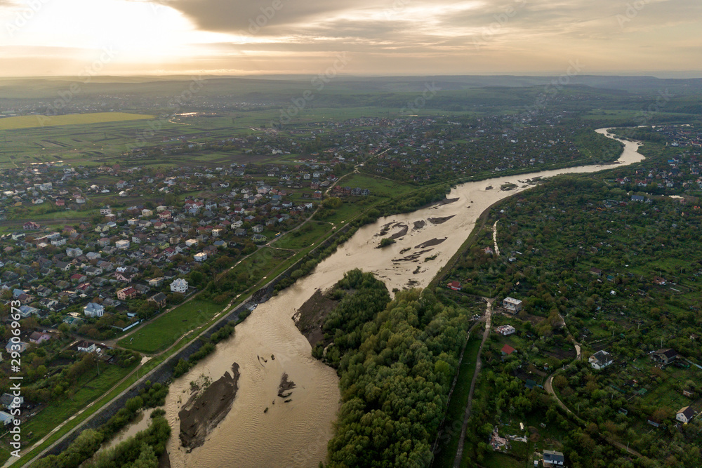 Aerial landscape of small town or village with rows of residential homes and green trees and big flloded river.