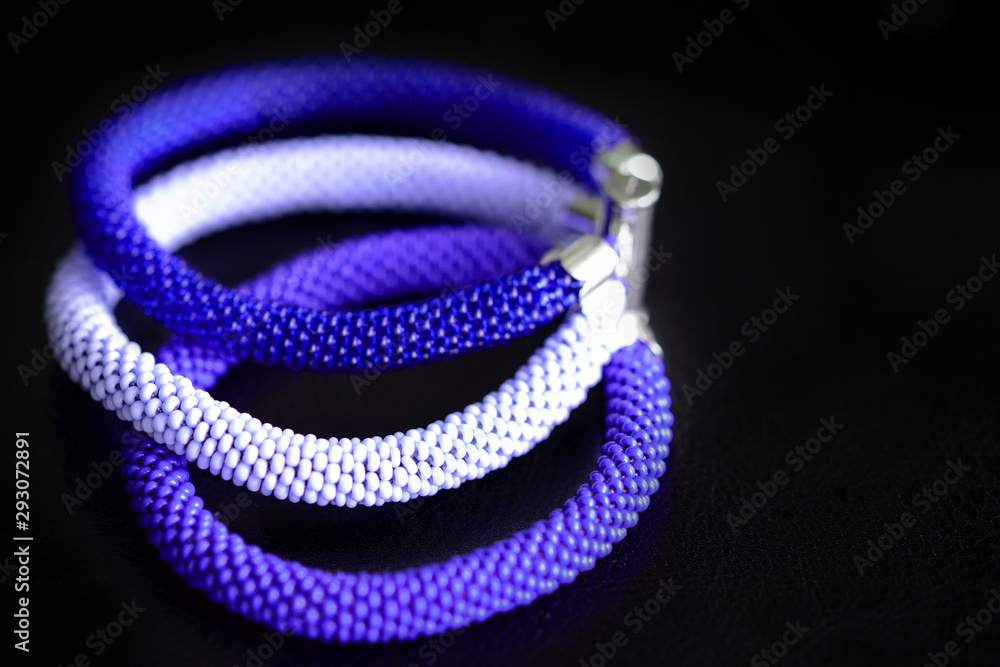 Fototapeta premium Beaded bracelet of three crocheted ropes on a dark background close up
