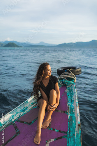 Young woman relaxing on the boat at sunset and looking at the island. Old traditional asian boat, travel in Indonesia