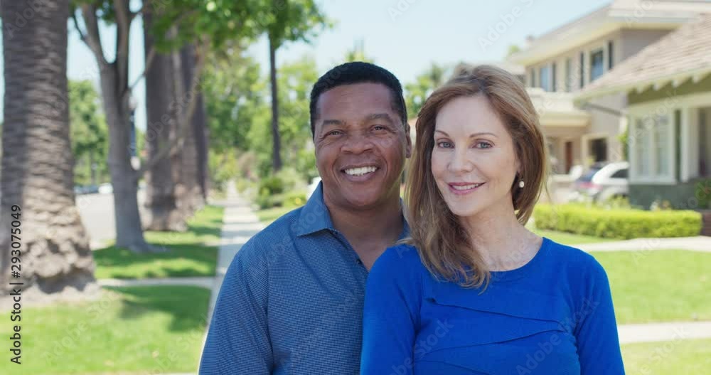 Portrait of senior African American and Caucasian couple smiling on sidewalk in suburban neighborhood. Happy older husband and wife homeowners looking at camera. Slow Motion 4k Handheld Portrait of senior African American and Caucasian couple smiling on sidewalk in suburban neighborhood. Happy older husband and wife homeowners looking at camera. Slow Motion 4k Handheld