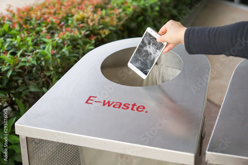 Hand dropping an old, damaged smartphone into a bin for e-waste garbage