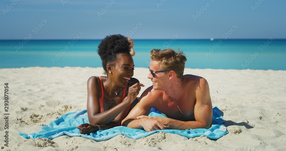 A happy young different ethnicity couple is having fun to apply a sunscreen or sun tanning lotion to take care of their skin during a vacation on a beach. A happy young different ethnicity couple is having fun to apply a sunscreen or sun tanning lotion to take care of their skin during a vacation on a beach.