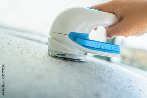 Canvas Print Fabric shaver fuzz remover woman removing lint on clothes at home with handheld electric defuzzer