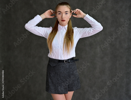 Portrait of a pretty manager girl in a white shirt and gray skirt on a gray background with long hair. Great makeup, beautiful face. It is in different poses with different emotions.