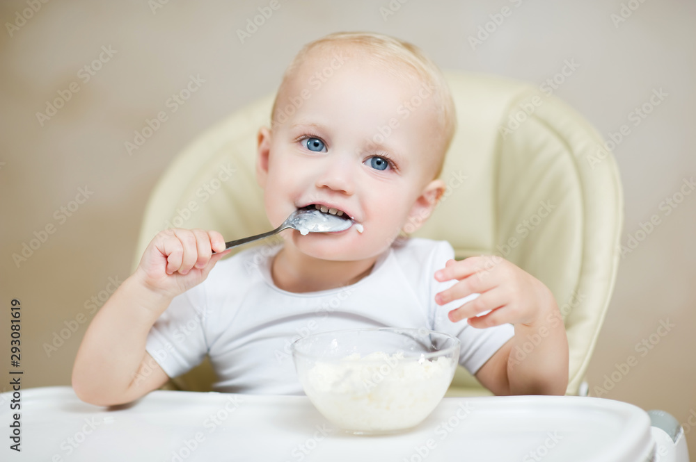 cute baby boy in a chair holds a spoon in his mouth and smiles cute baby boy in a chair holds a spoon in his mouth and smiles
