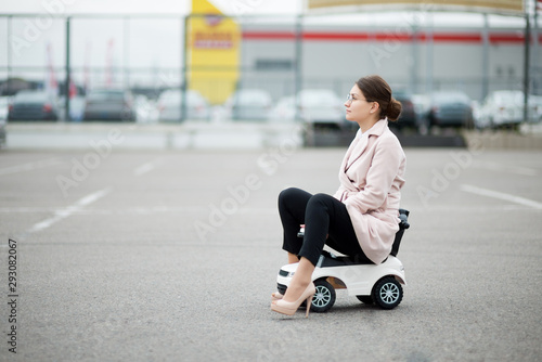 Εκτύπωση καμβά girl in a coat and trousers sits on a plastic car in a supermarket parking lot a