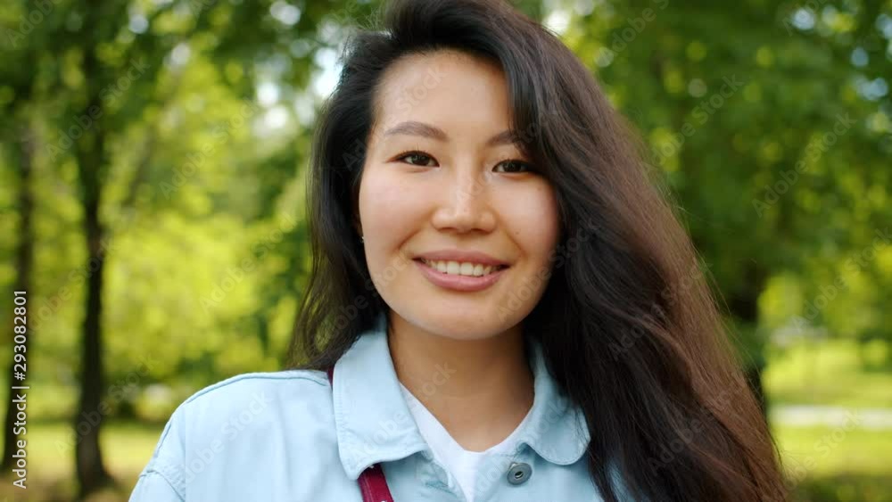 Beautiful Asian woman student is standing outdoors in green park alone smiling looking at camera. Happy people, positive emotions and nature concept. Beautiful Asian woman student is standing outdoors in green park alone smiling looking at camera. Happy people, positive emotions and nature concept.