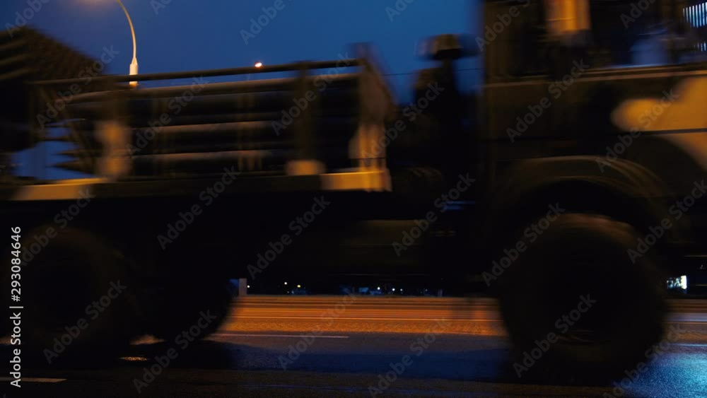 A convoy of military equipment rides through the city at night with headlights on A convoy of military equipment rides through the city at night with headlights on
