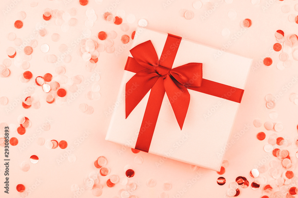 Gift box with confetti on coral background.