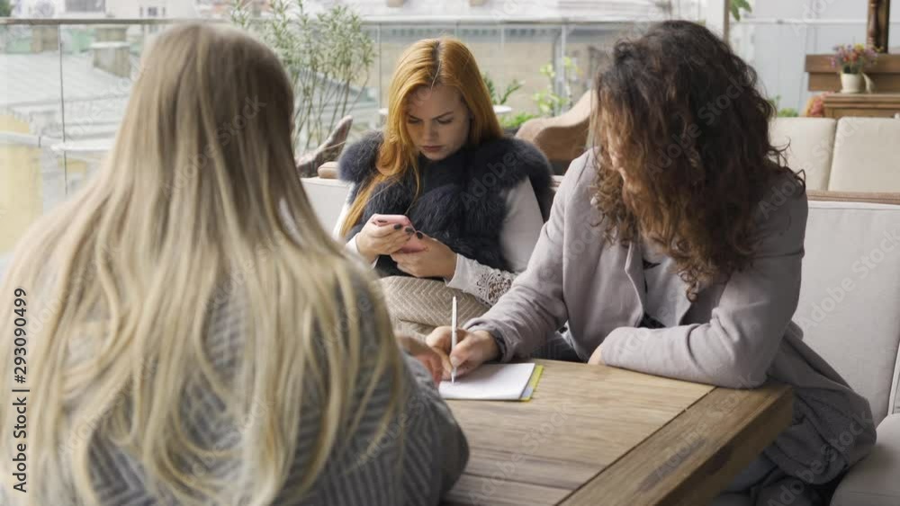 custom made wallpaper toronto digitalThree caucasian girlfriends sitting at the table in the cafe. One girl using phone while two friends talking. Young women relaxing together indoors. Autumn leisure. Friendly meeting