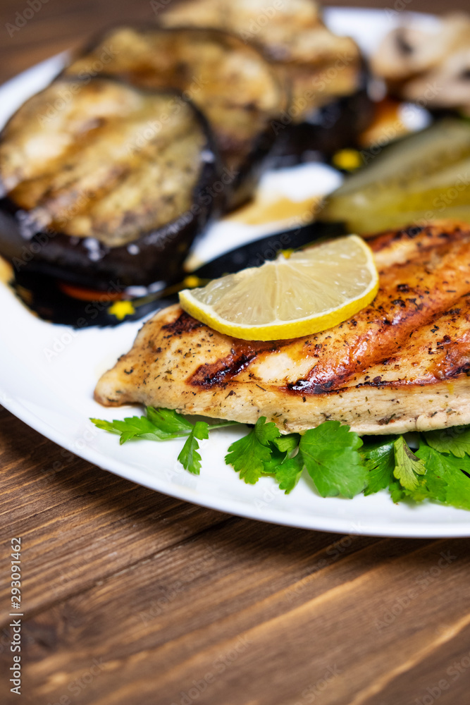 Delicious grilled chicken fillet and eggplant on a plate. Dark wooden table as a background