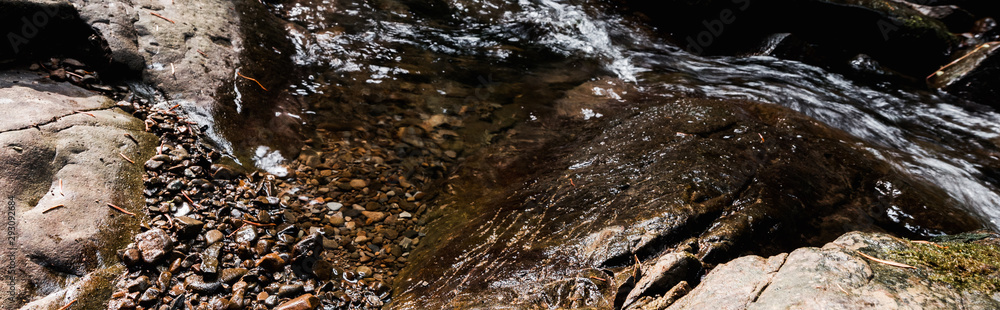 panoramic shot of sunshine on flowing river near wet stones in park panoramic shot of sunshine on flowing river near wet stones in park