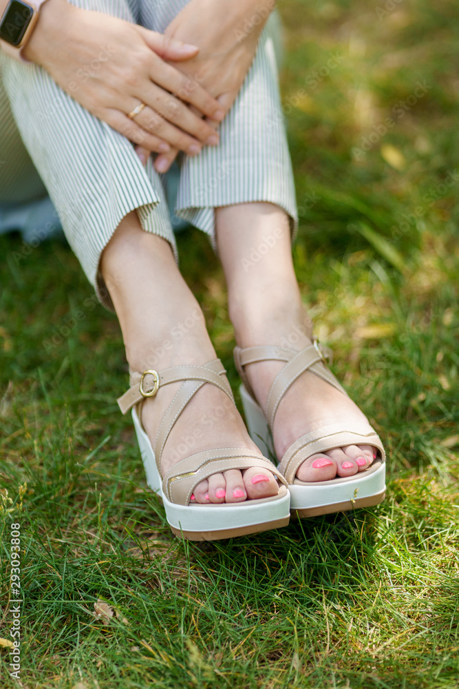 A woman's feet in summer shoes and stripped pants standing on the green grass