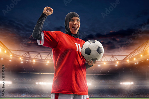 Female muslim soccer player in hijab standing with a ball on a professional stadium photo