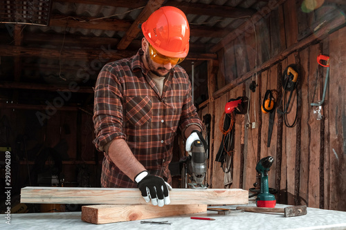 A man carpenter cuts a wooden beam using an electric jigsaw, male hands with an electric jigsaw closeup. Work with wood.