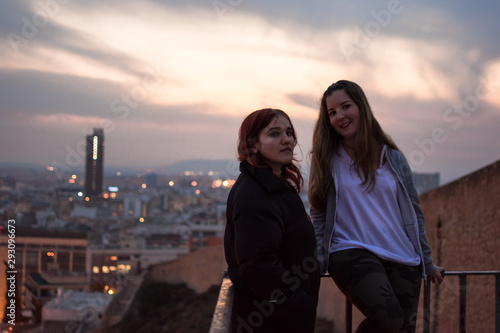 Two young women talking looking the lights of the city in a rooftop © Cristian Blázquez