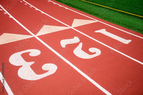 Bright sunny view of athletic running track in fresh red rubber with numbered lanes © lazyllama